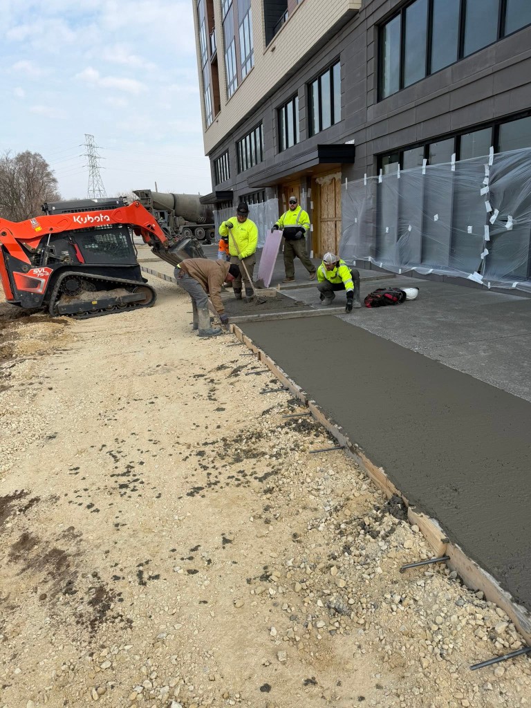 Crew pouring and finishing concrete beside equipment on a jobsite